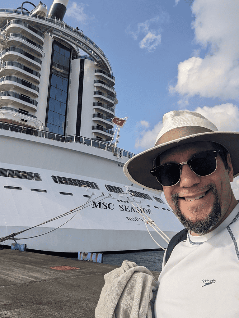 Luxury cruise ship MSC Seaside docked at port with man in hat and sunglasses in foreground, travel and vacation concept.