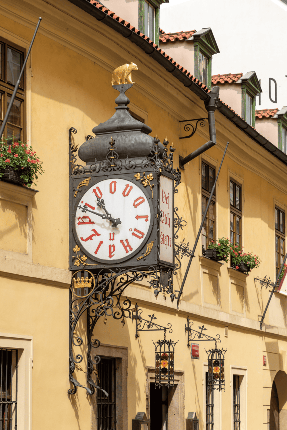 1. Vintage European street clock with ornate metalwork and flower boxes in sunny town.