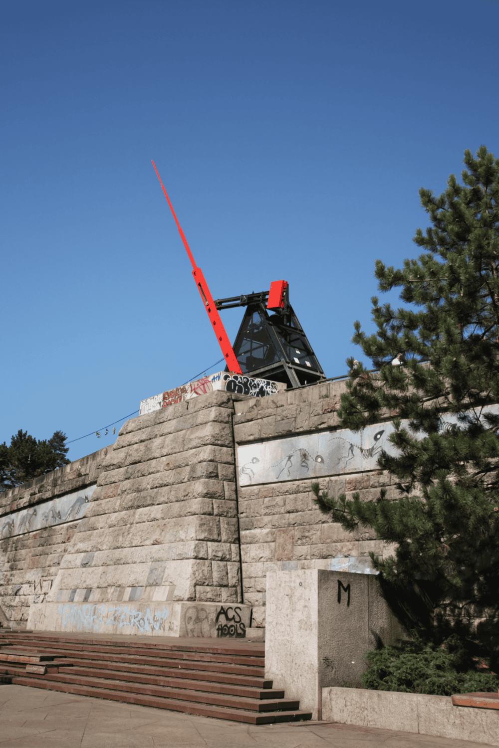 Colorful tram cable car tower against a blue sky with graffiti on the stone wall and steps in the foreground.