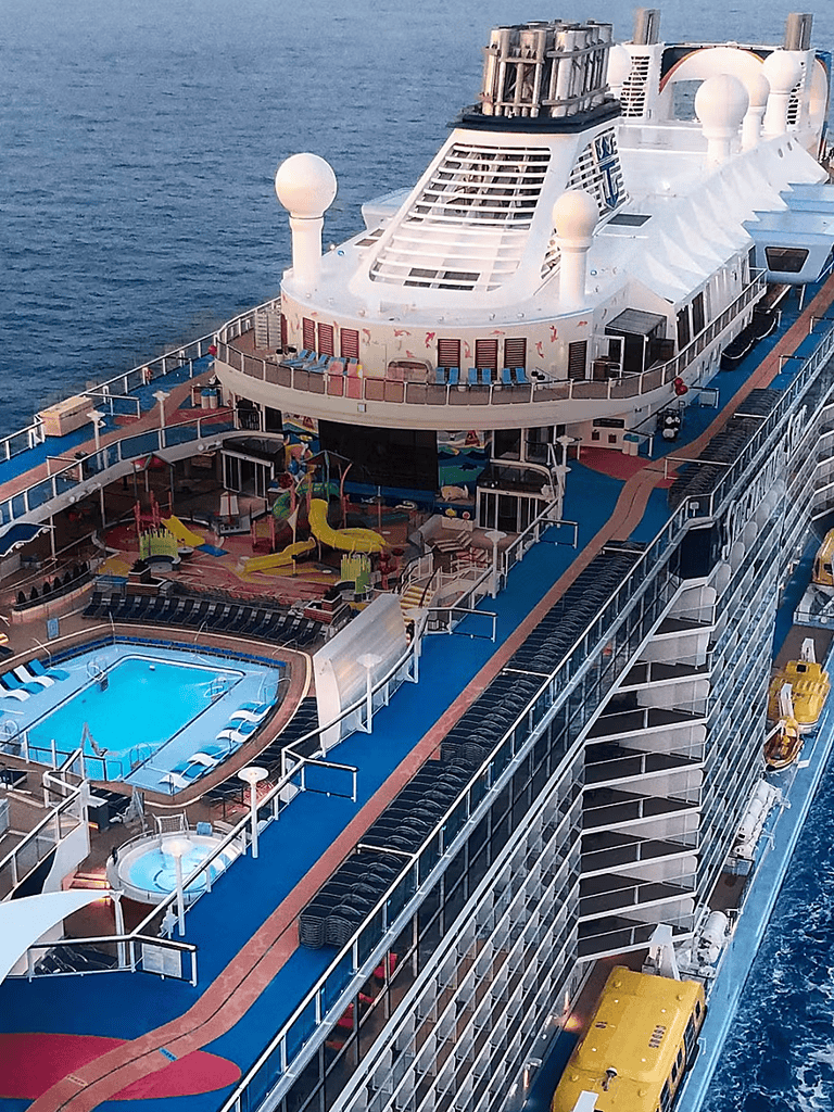 Vast cruise ship with pools, water slides, and outdoor lounge areas at sea.
