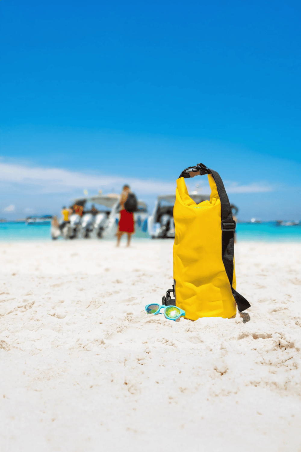 Bright yellow waterproof backpack and swimming goggles on sandy beach, sunny day.