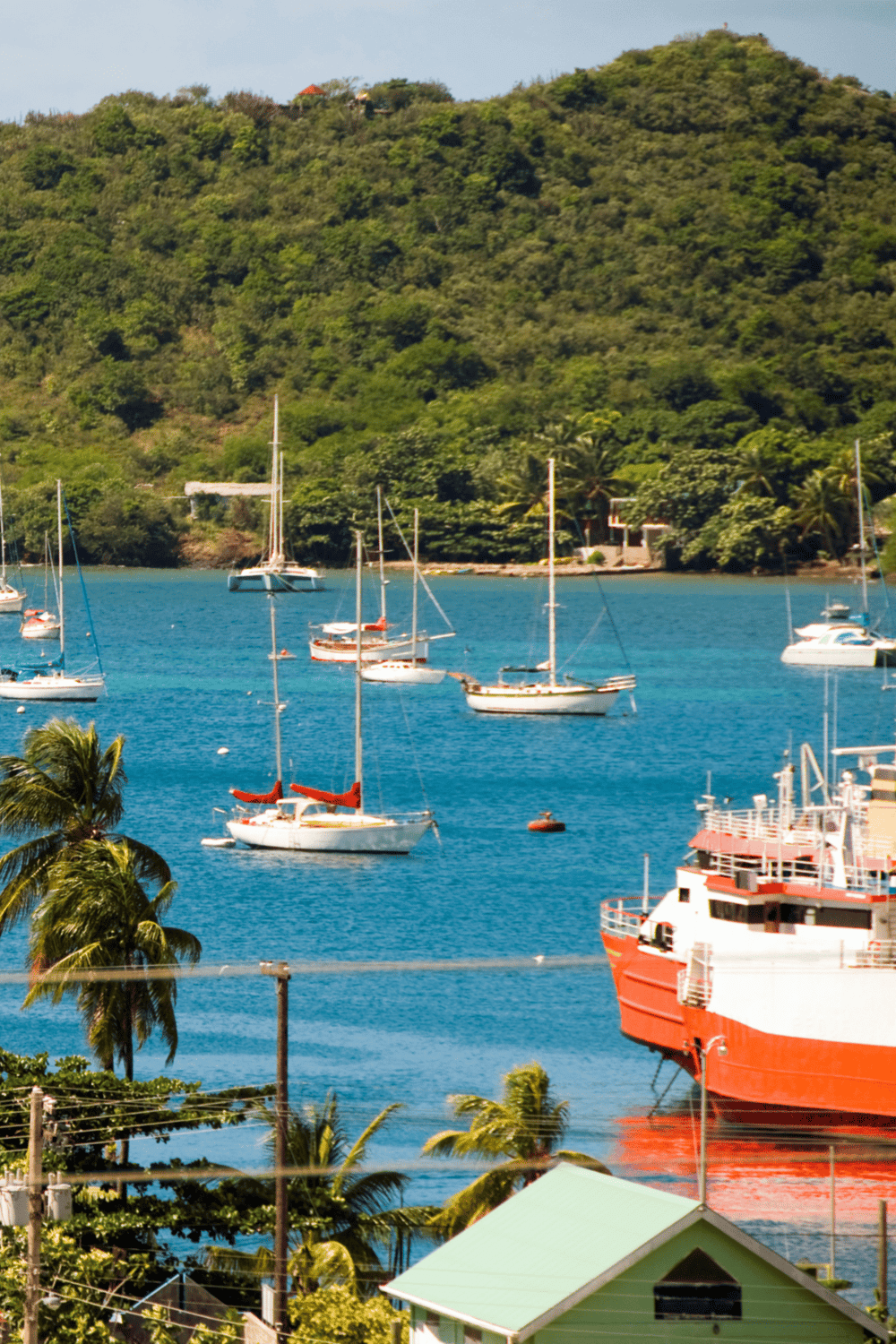 Boats anchored on a vibrant blue bay with lush green hills in the background, showcasing tropical seaside scenery.