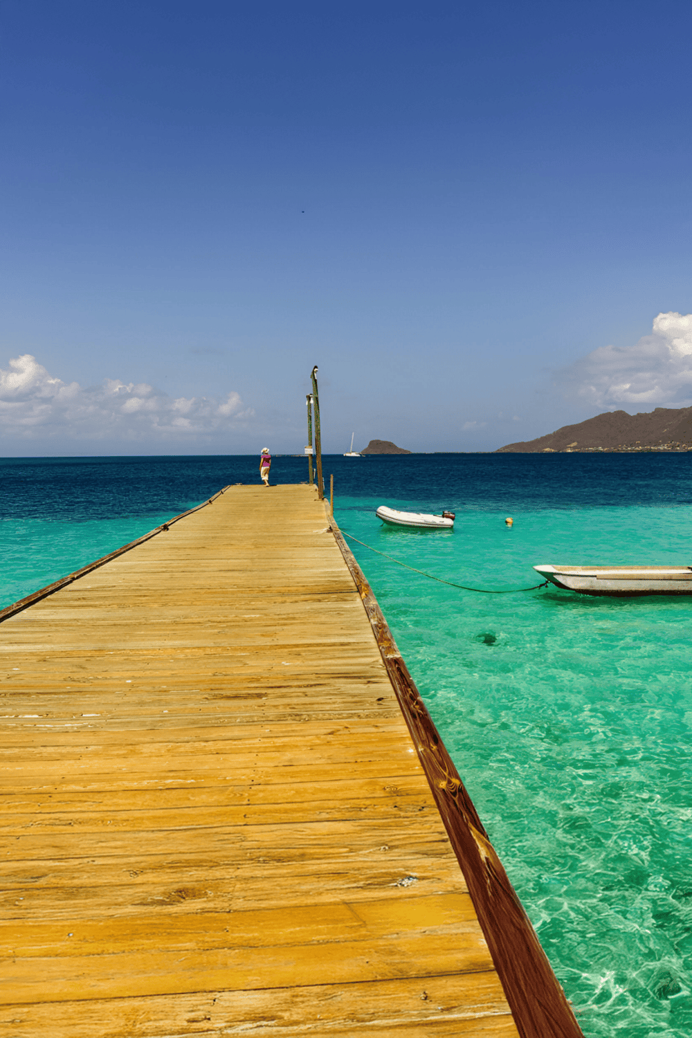 Seaside wooden pier with boats and clear turquoise water, scenic ocean view, tropical vacation destination.