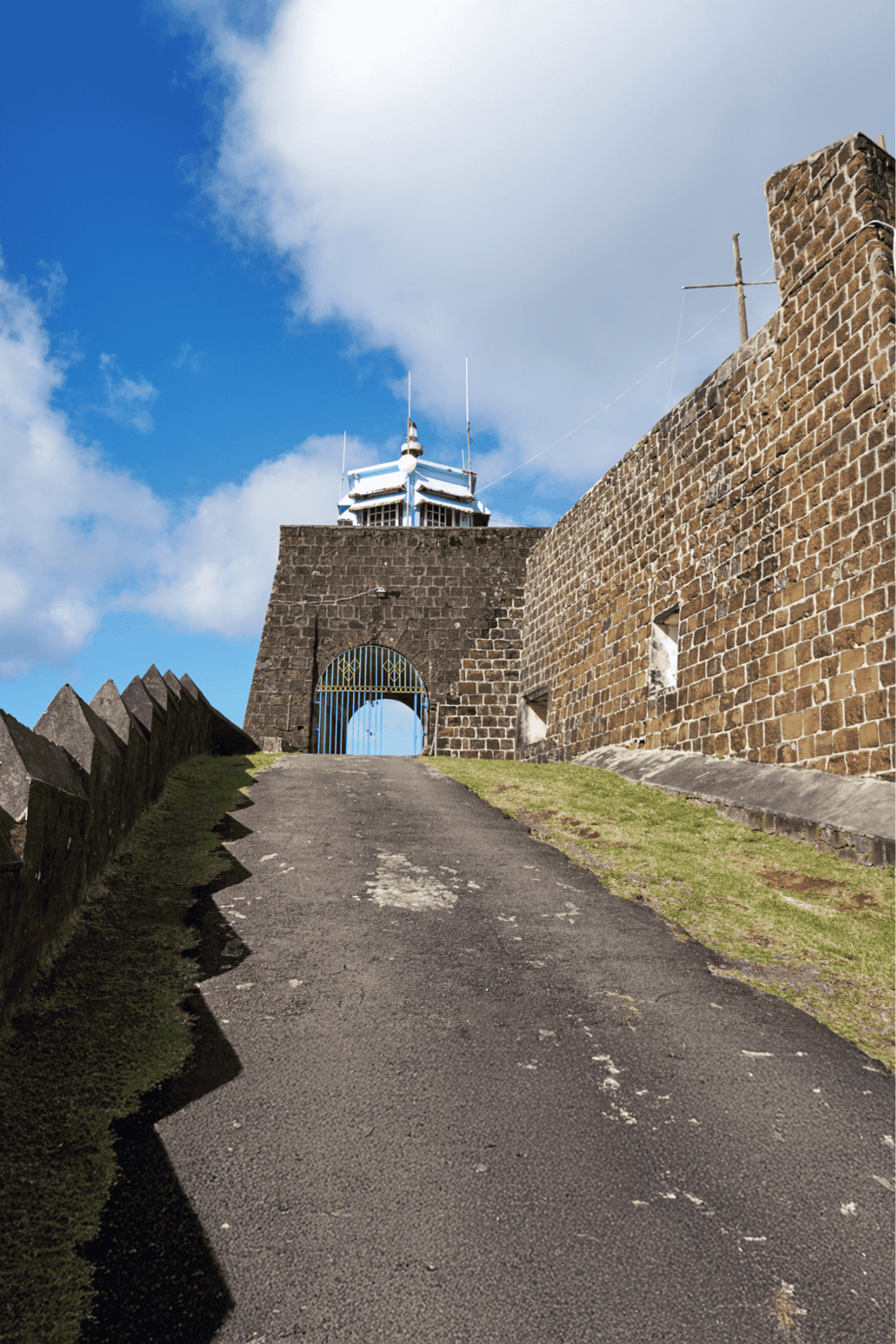 Queen's Wharf Castle entrance with blue sky and clouds, historic stone walls, and a gated pathway.