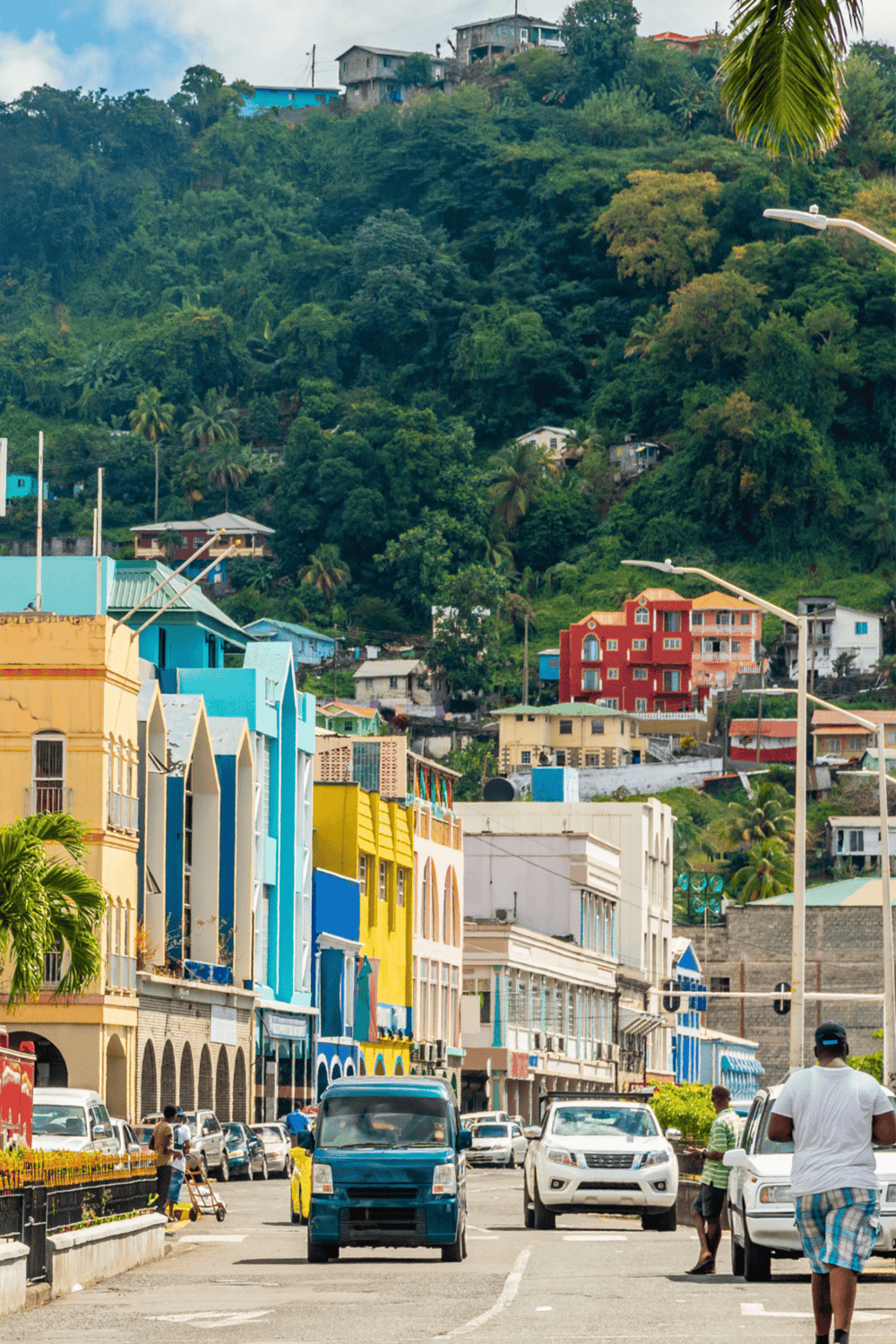 Colorful city street with vibrant buildings and lush green hillside in the background.