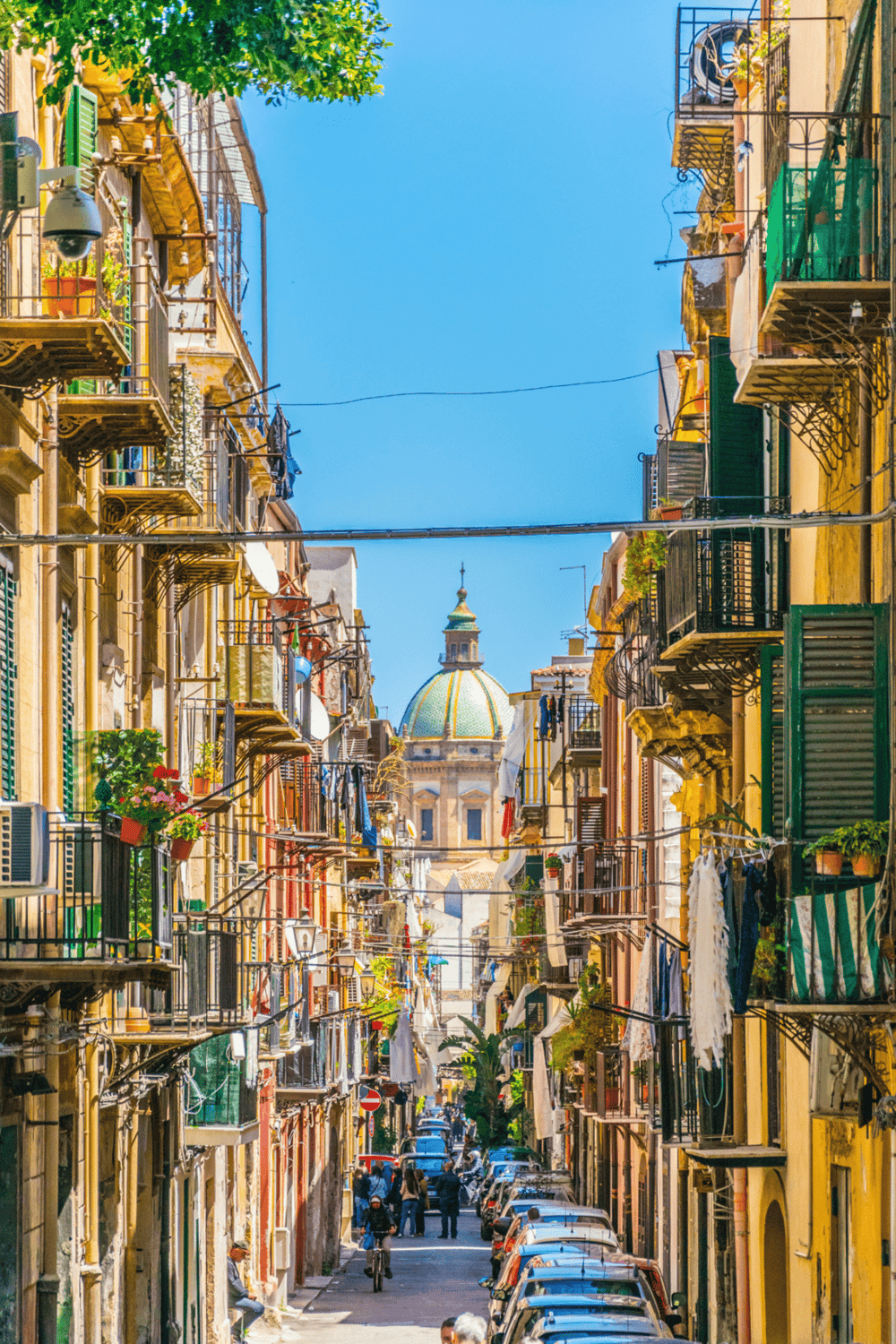 Colorful Naples street with balconies, laundry, and a historic dome in the background, showcasing Italy's vibrant cityscape.