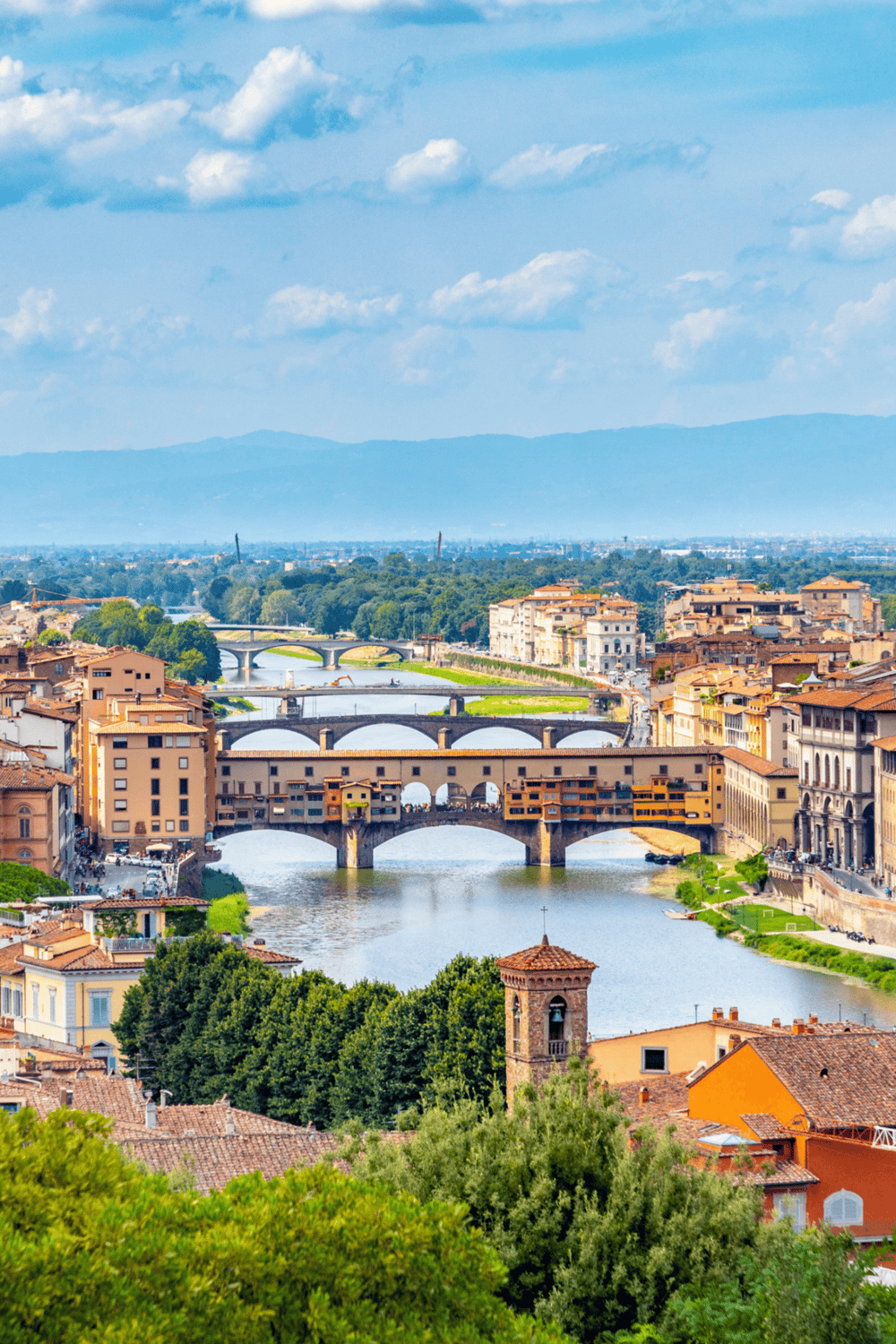 Historic Florence Ponte Vecchio river bridge in Italy under blue sky with clouds.