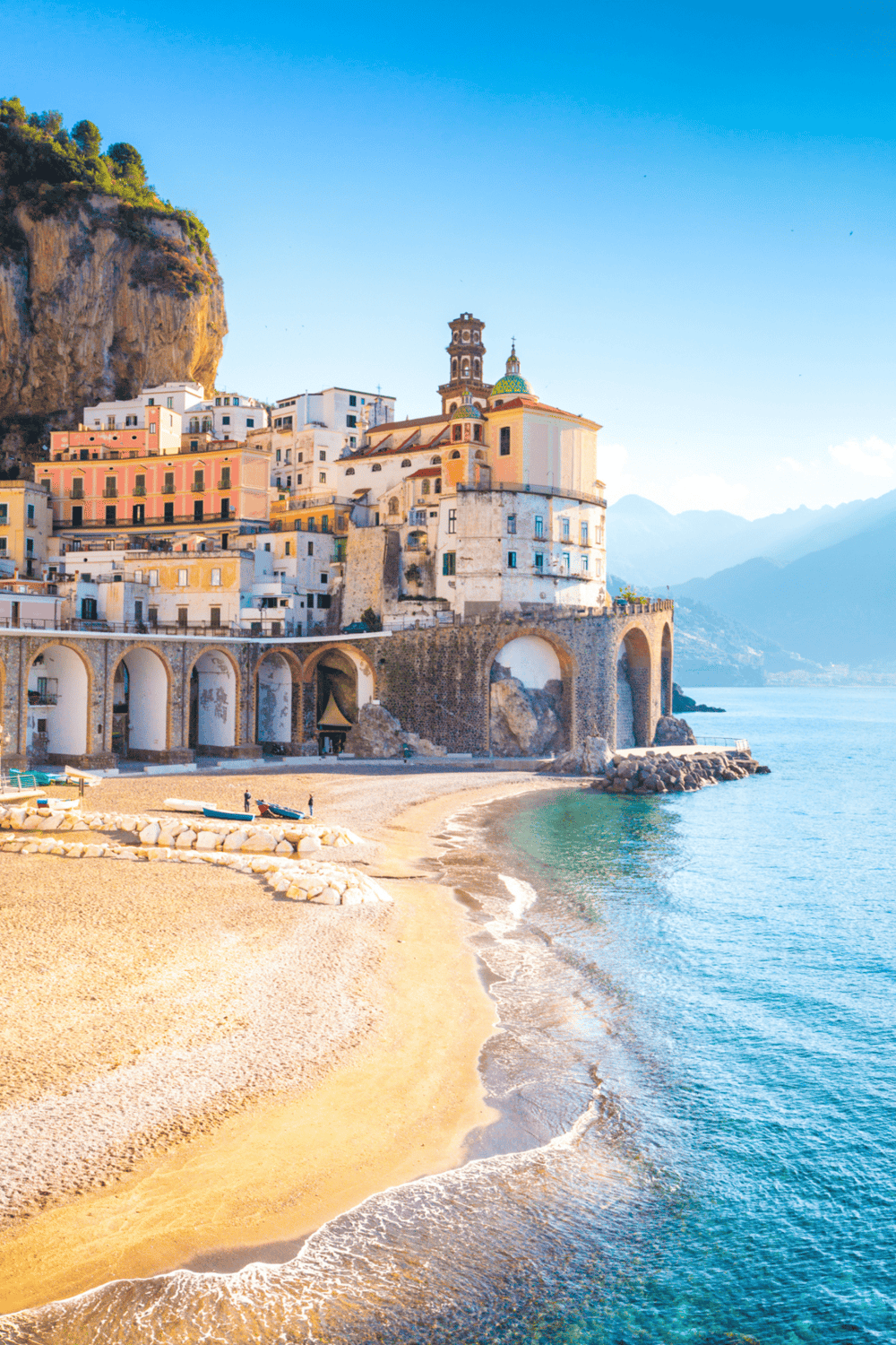 Cliffside coastal town with colorful buildings, beach, and mountains, in Italy's Amalfi Coast.