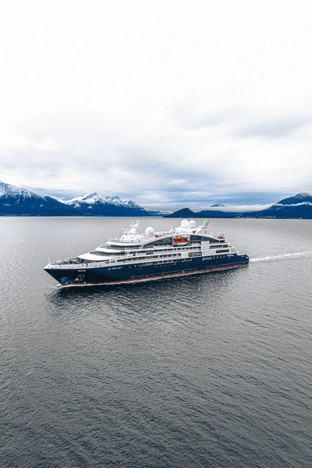 Luxury cruise ship navigating icy waters with snow-capped mountains in the background.