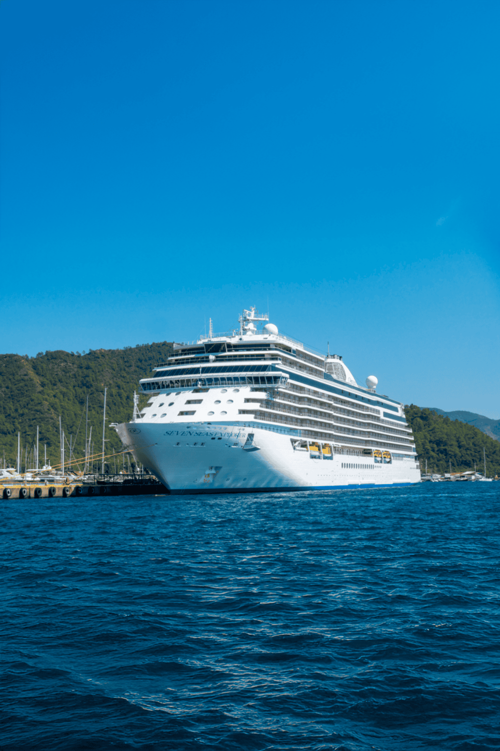 Luxury cruise ship docked at harbor on sunny day, exploring ocean travel options.