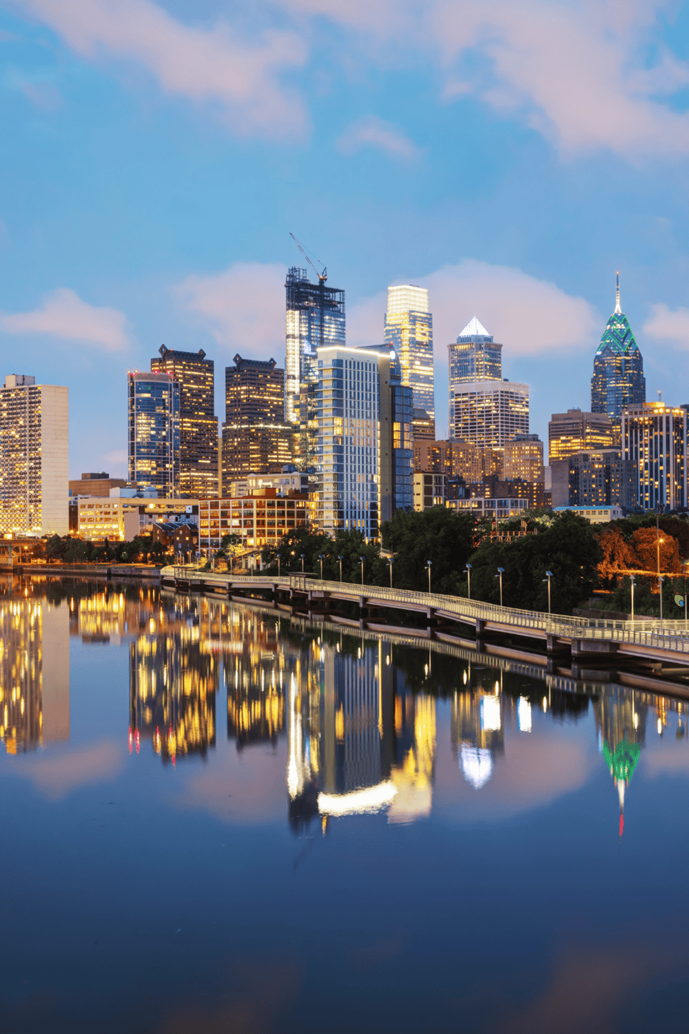 Vibrant downtown skyline of Philadelphia with illuminated skyscrapers and their reflection on the Delaware River at dusk.