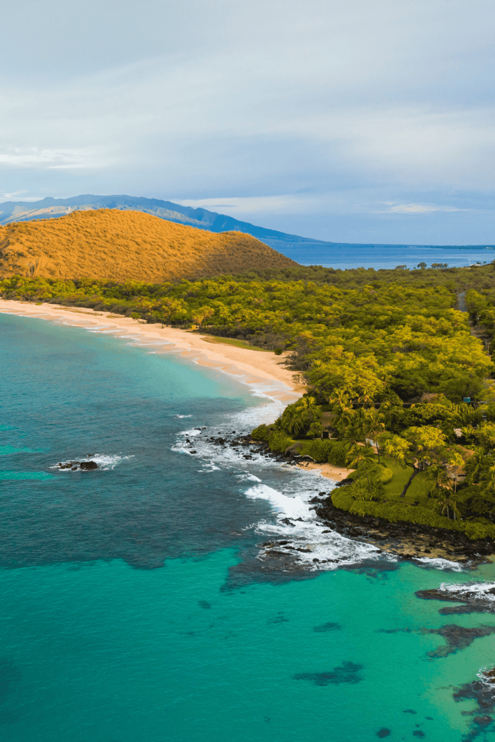 Aerial view of a tropical coastline with lush greenery, sandy beach, and turquoise waters, highlighting travel and beachfront vacation spots.