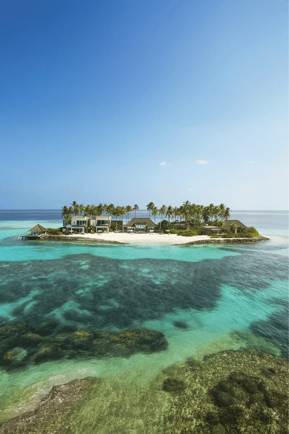 Luxurious island resort with overwater bungalows, palm trees, turquoise waters, and white sandy beaches.