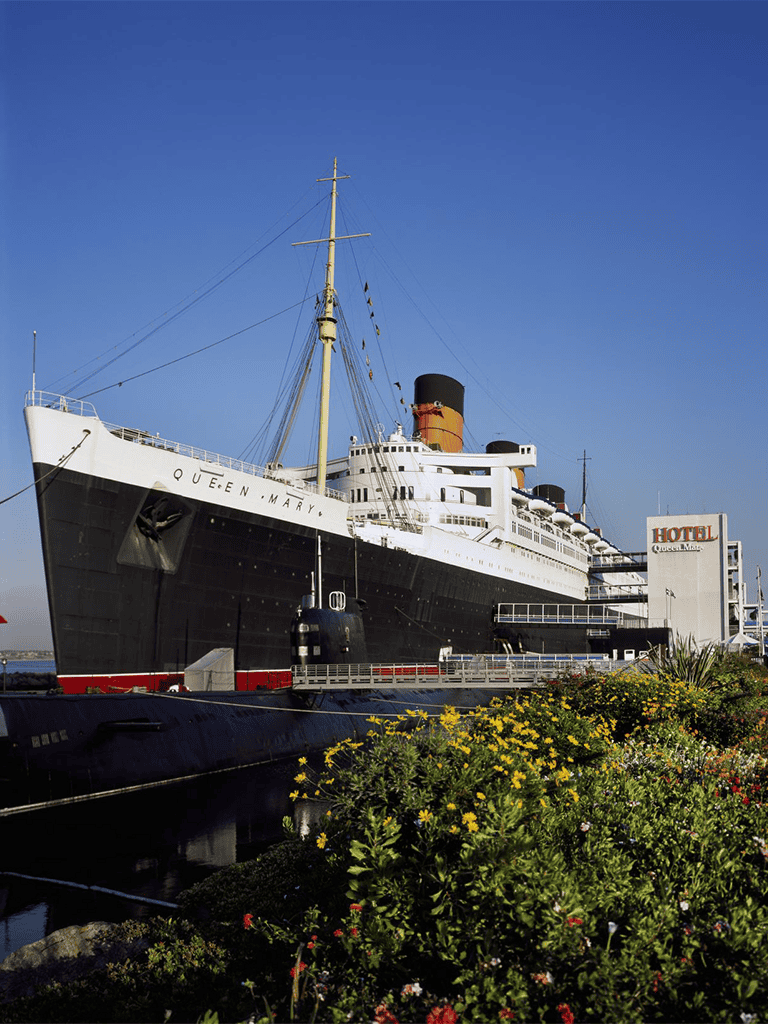 Queen Mary ocean liner at dock with vibrant flowers in foreground.