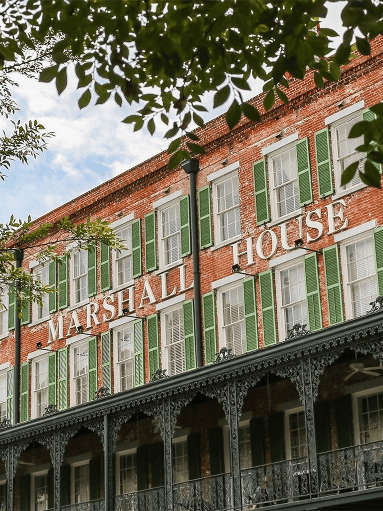 Charming historic Marshall House with green shutters and decorative iron balcony in Savannah, GA.
