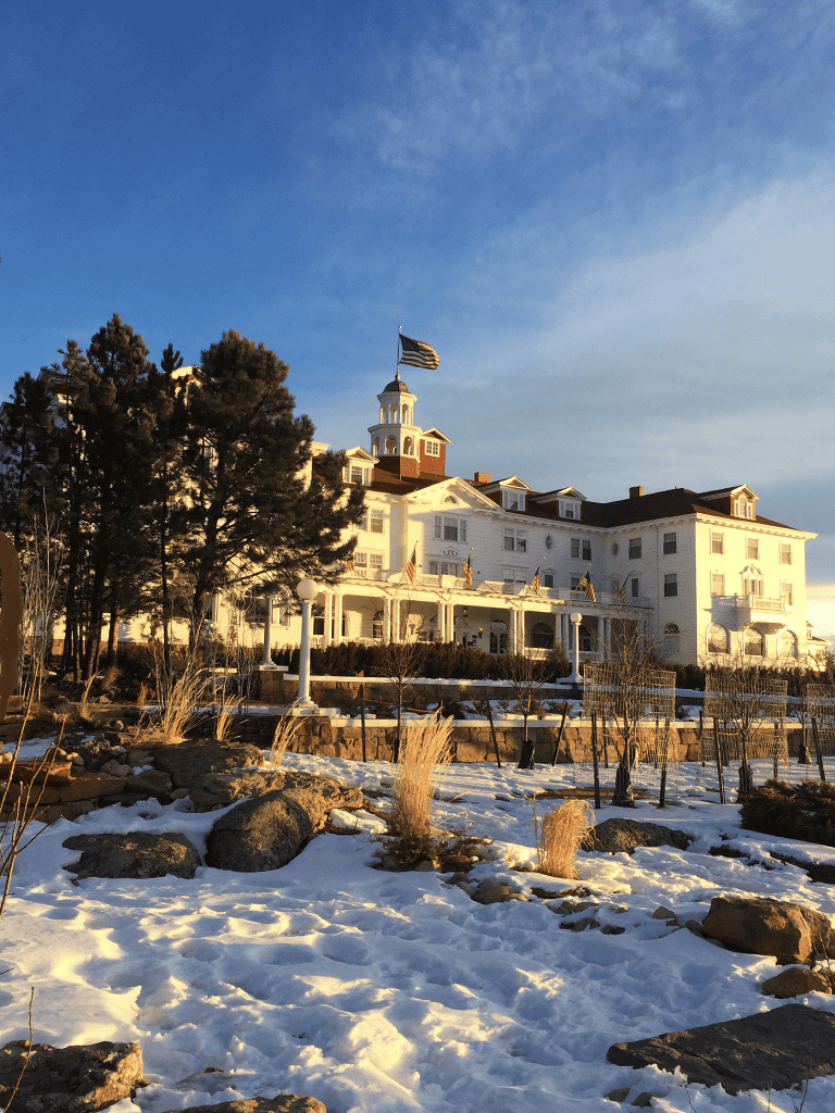 Elegant white historic hotel with a flagpole, situated on a snow-dusted landscape during sunset.