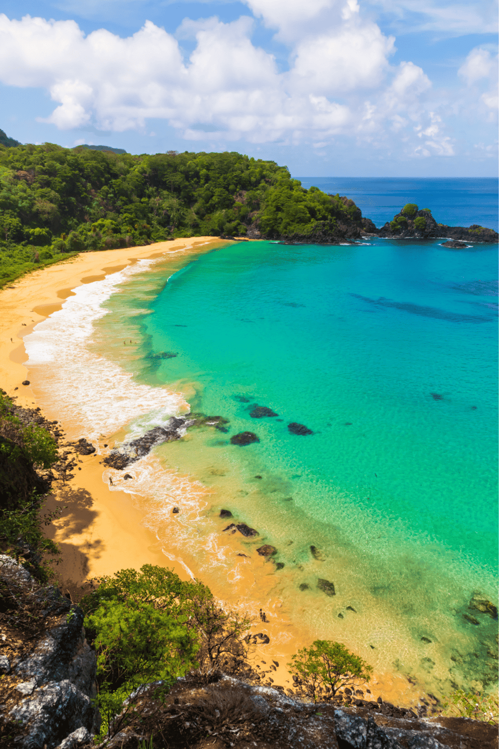 Turquoise beach with lush green hills and rocky shoreline, tropical paradise destination.