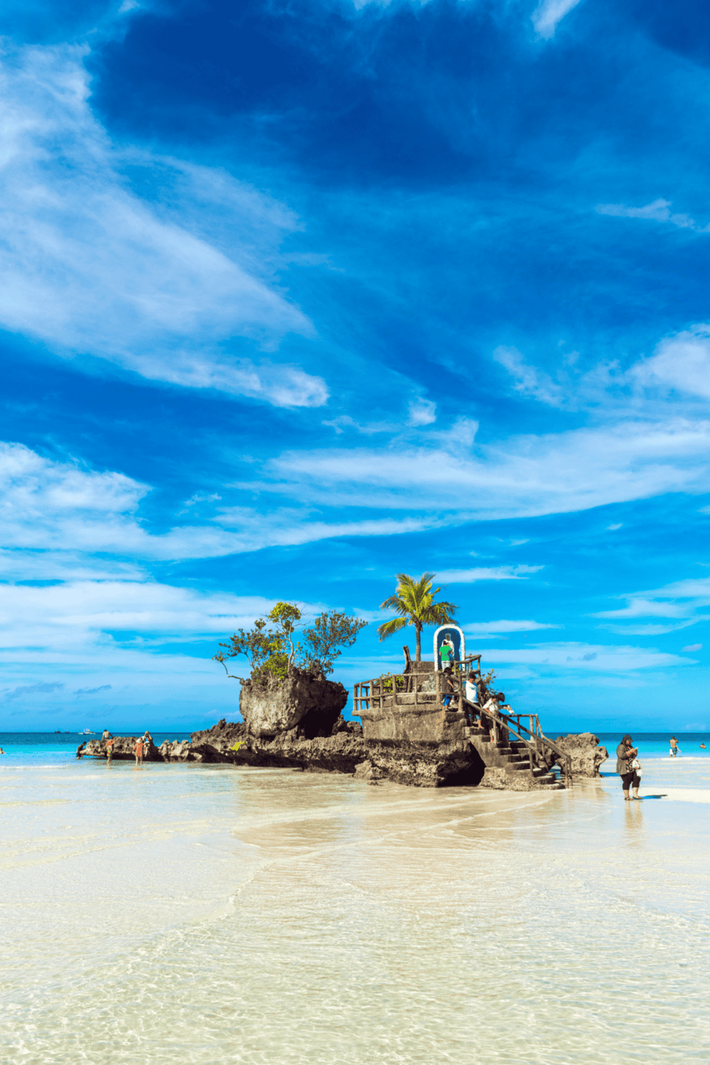 Vibrant tropical beach with rock formation, palm trees, and clear blue sky, perfect for travel and vacation photos.