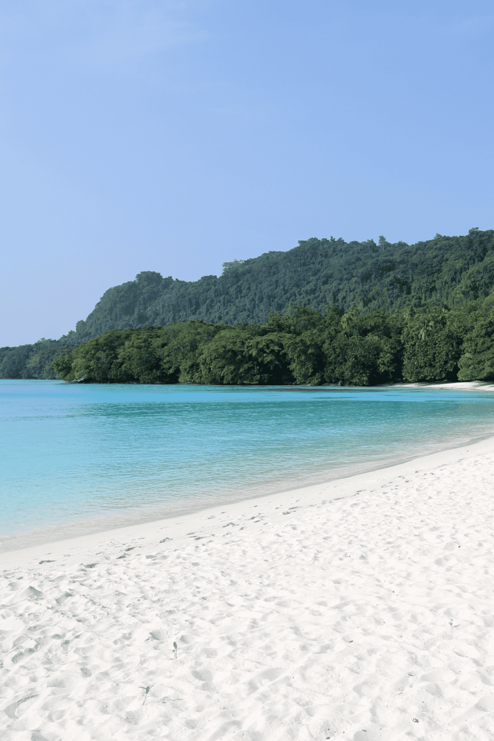Serene tropical beach with turquoise waters and lush green island backdrop.