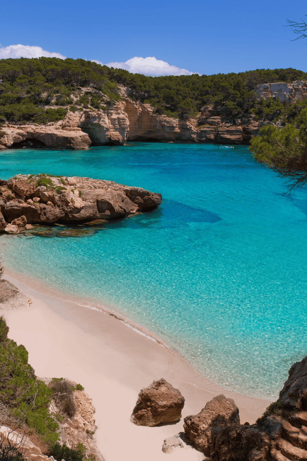Crystal clear turquoise waters at secluded island cove with sandy beach and rocky cliffs.