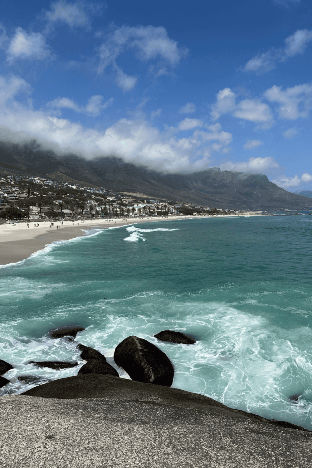 Stunning Cape Town beach with mountains, blue sky, and ocean waves.