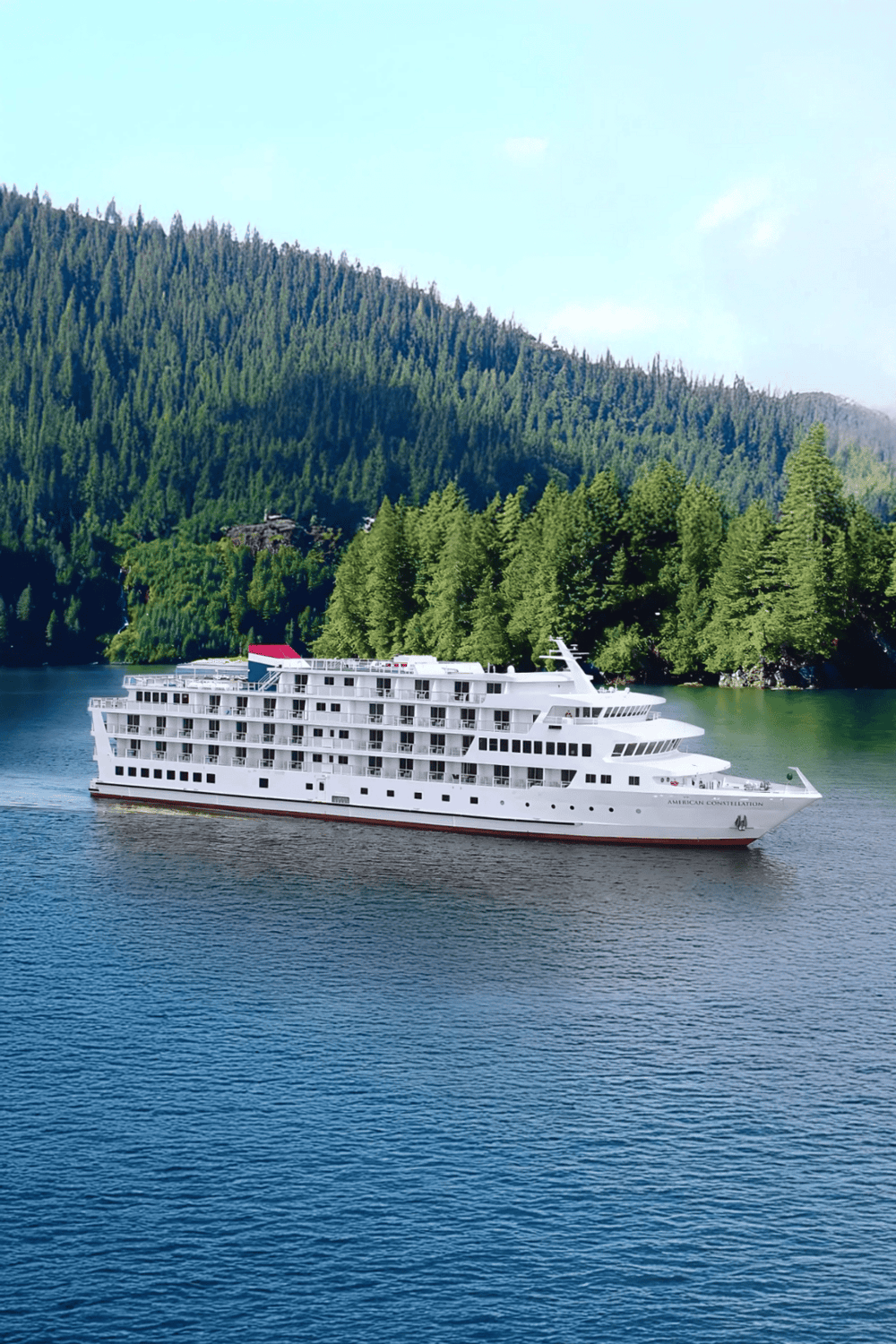 Luxury cruise ship on scenic waterway surrounded by lush green mountains.