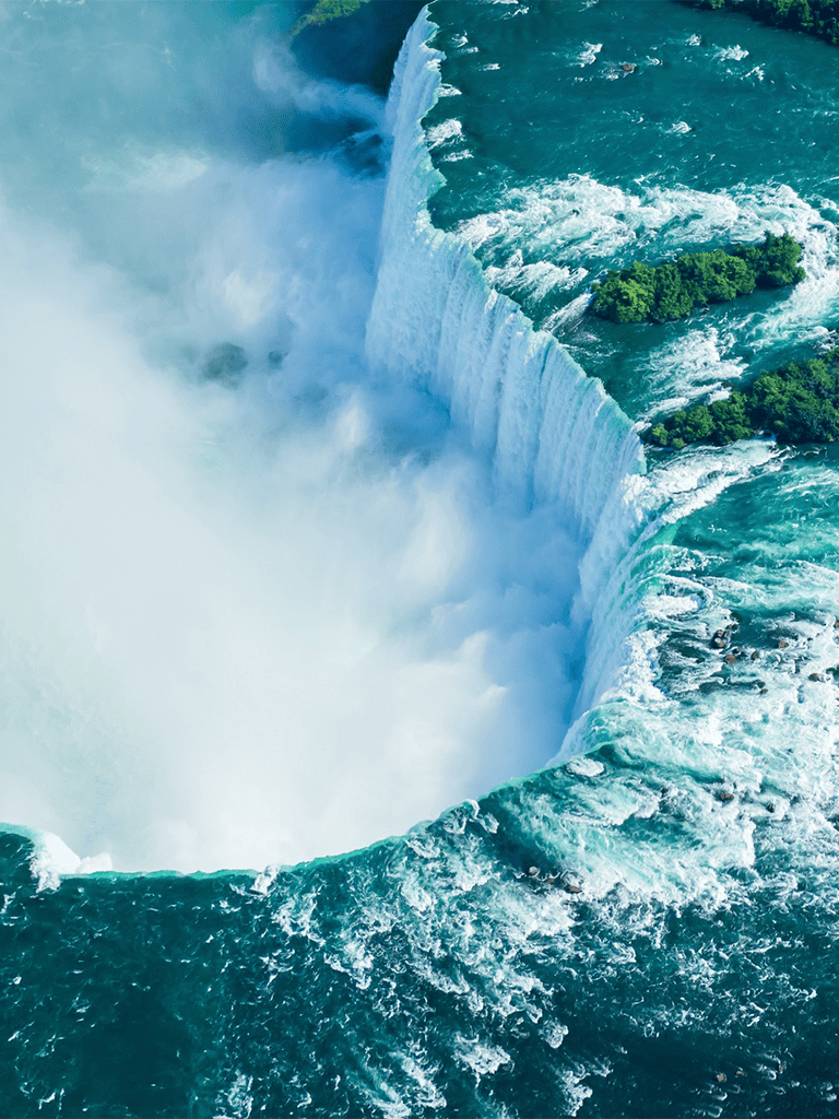 Vast Niagara Falls with rushing water and lush greenery.