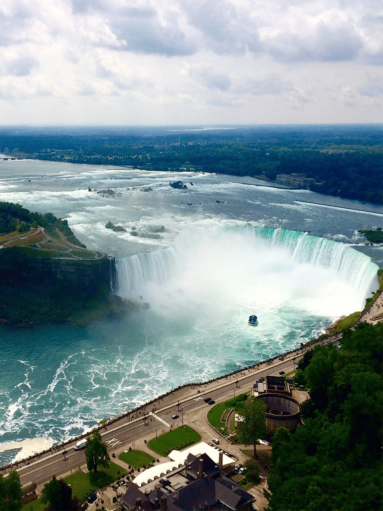 Image of niagara falls with boat in the water and parkway on the foreground.
