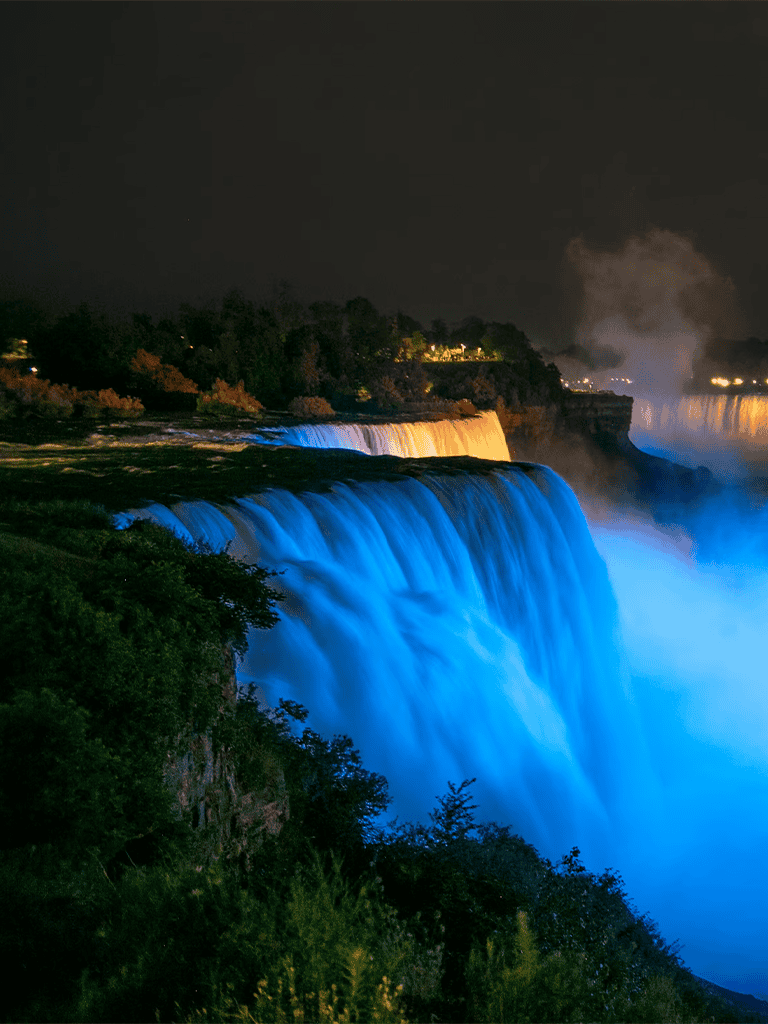 Night view of Niagara Falls illuminated with colorful lights.