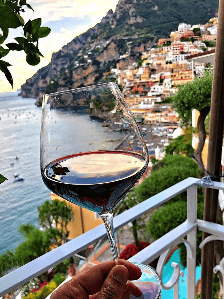 Breathtaking view of Positano coastline with a glass of red wine in the foreground, highlighting coastal travel and relaxation.
