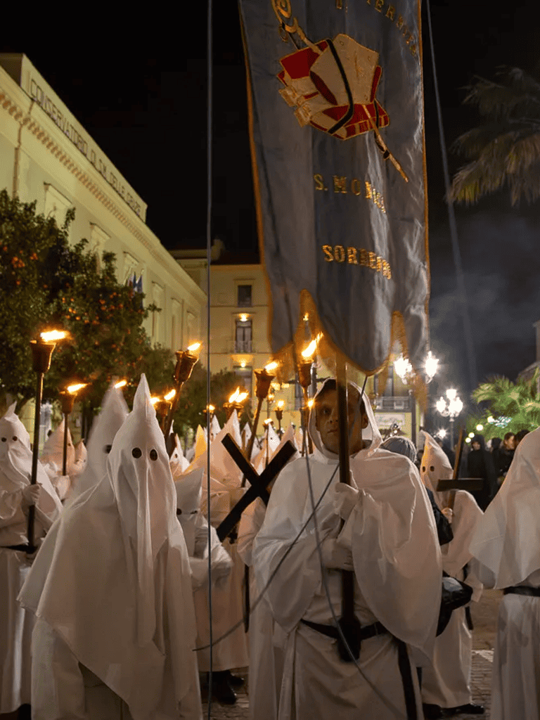 Children participating in a traditional Holy Week procession in Spain, dressed as Nazarenes with torches and banners.