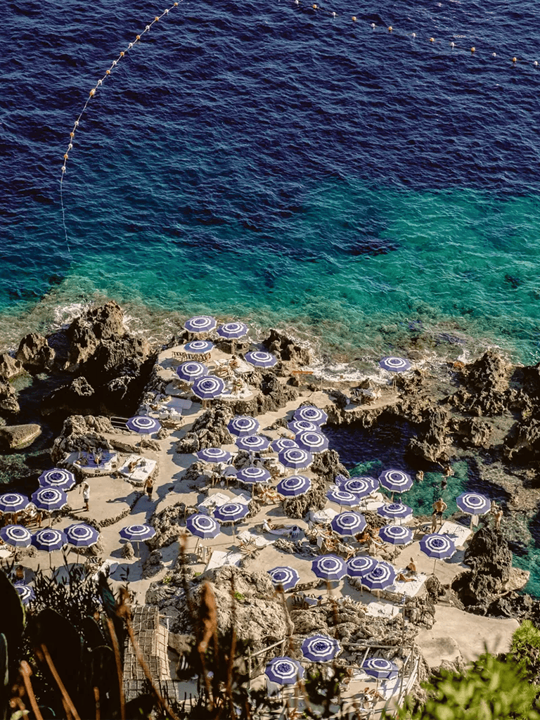 Elegant beach with blue umbrellas and rocky shoreline, perfect for seaside relaxation and sunbathing.