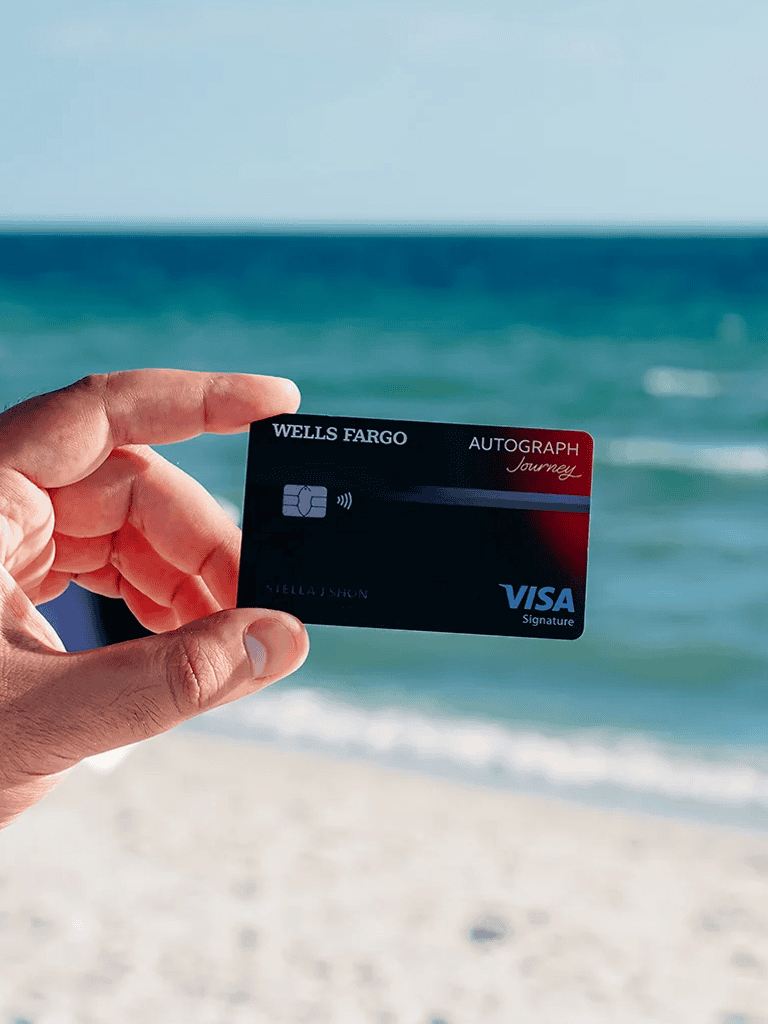 Wells Fargo Visa credit card held by hand near beach ocean background.