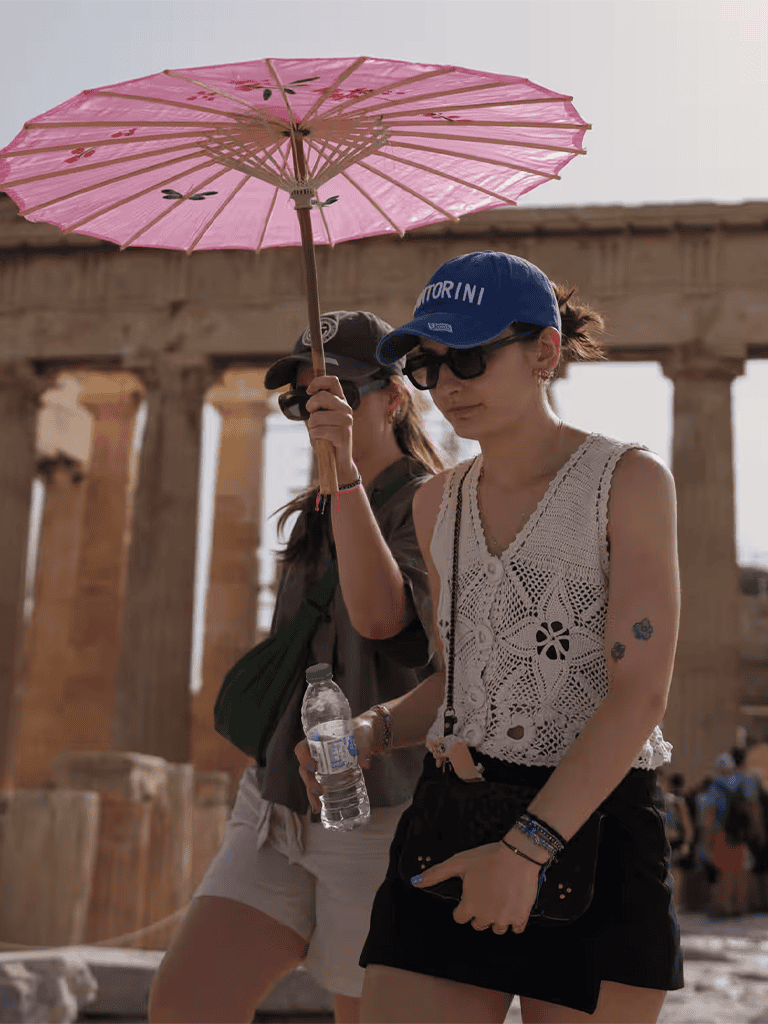 Pink parasol in front of ancient ruins with tourists, sunny day, travel, exploration, sightseeing, historical site.