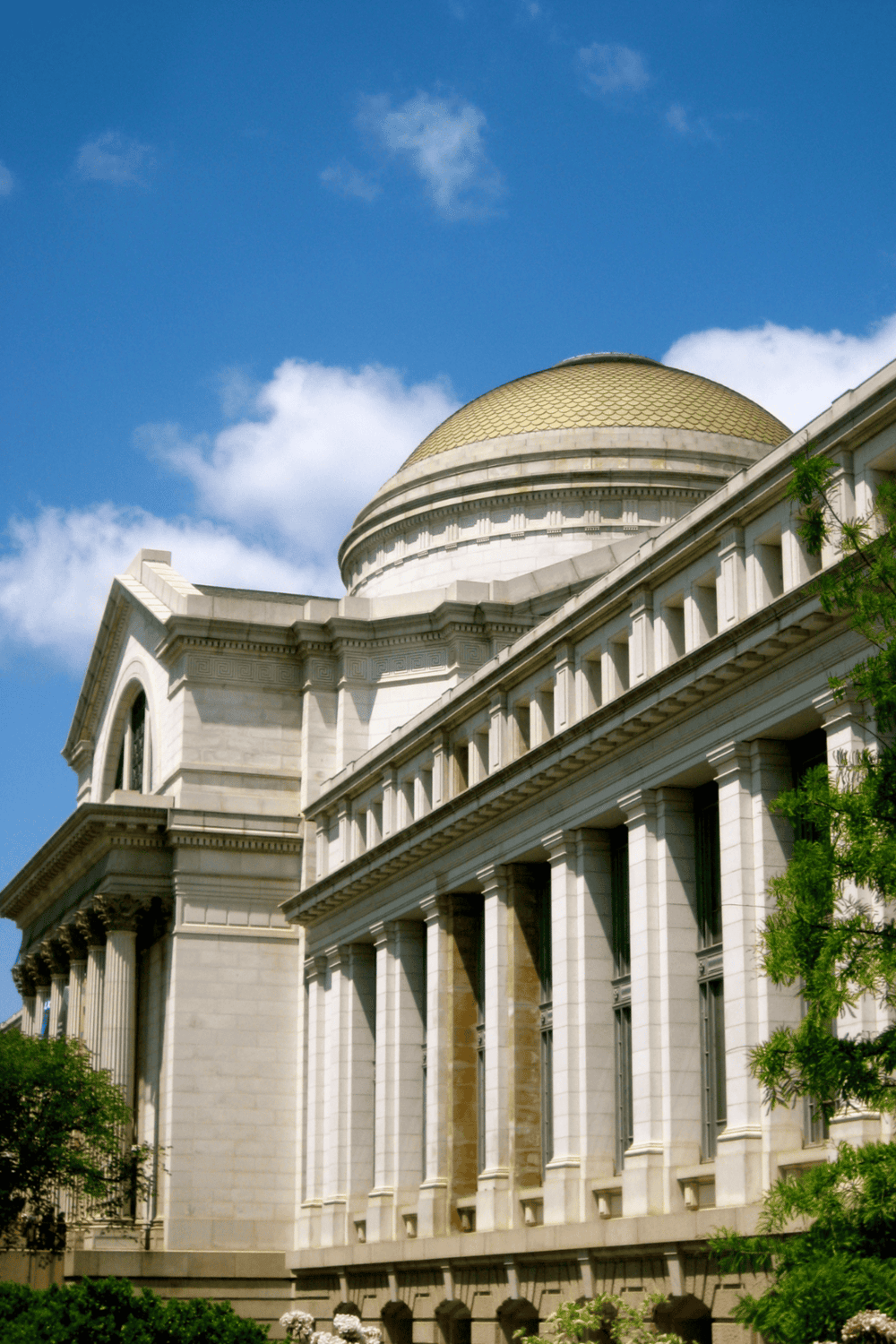 Elegant government building with classical architecture, white stone facade, and a prominent golden dome under blue sky.