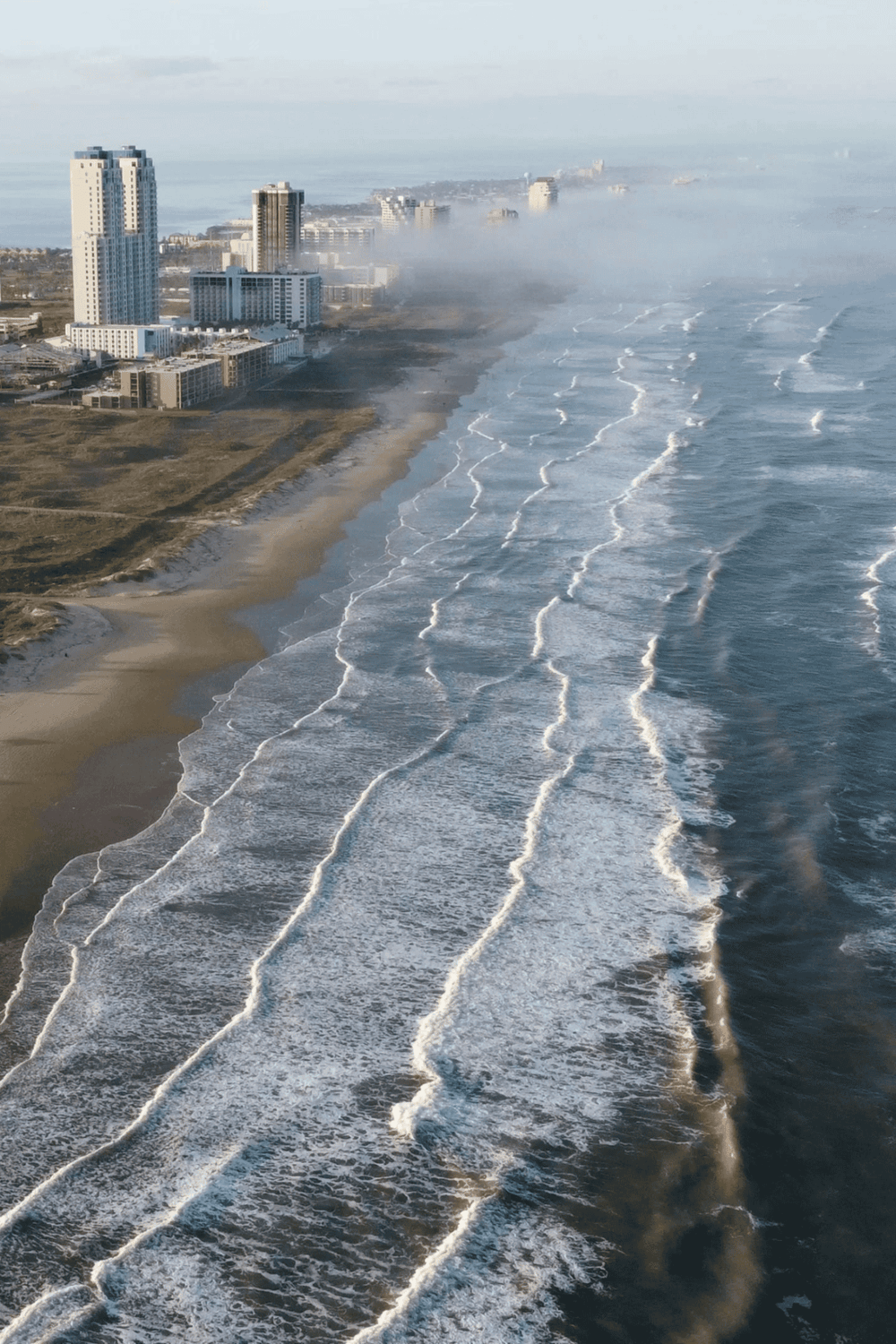 Aerial view of Miami Beach with high-rise buildings and ocean waves, showcasing coastal cityscape and beach access.