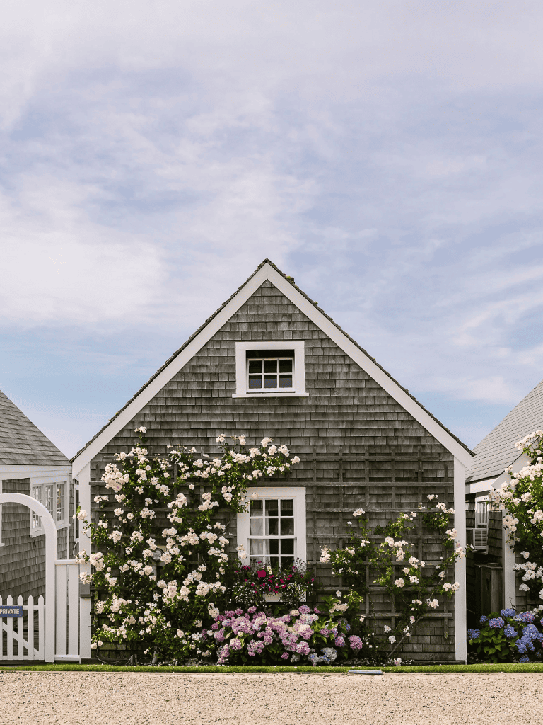 Charming beach house with floral garden, wooden shingles, and white trim, ideal for coastal living.