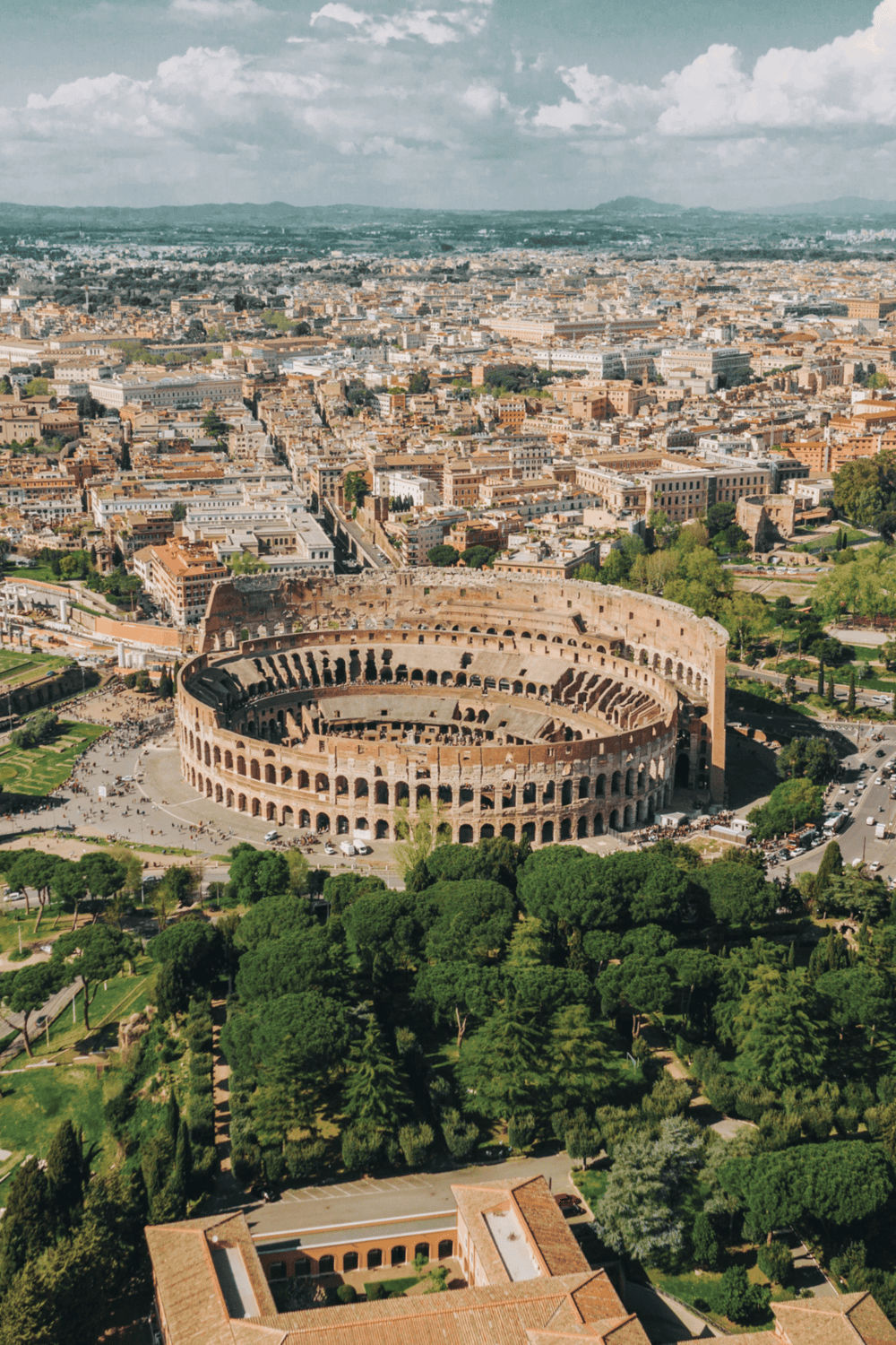 Ancient Roman Colosseum in Rome, Italy, surrounded by lush green parks and historic cityscape.