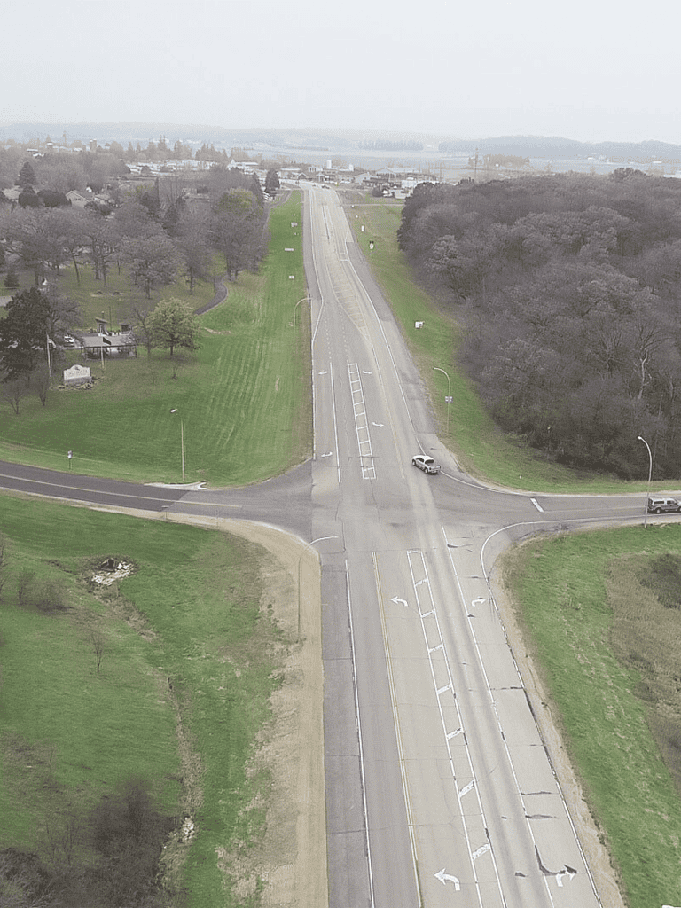 Aerial view of a rural road intersection with trees and green fields, promoting QuestForDirections navigation services.