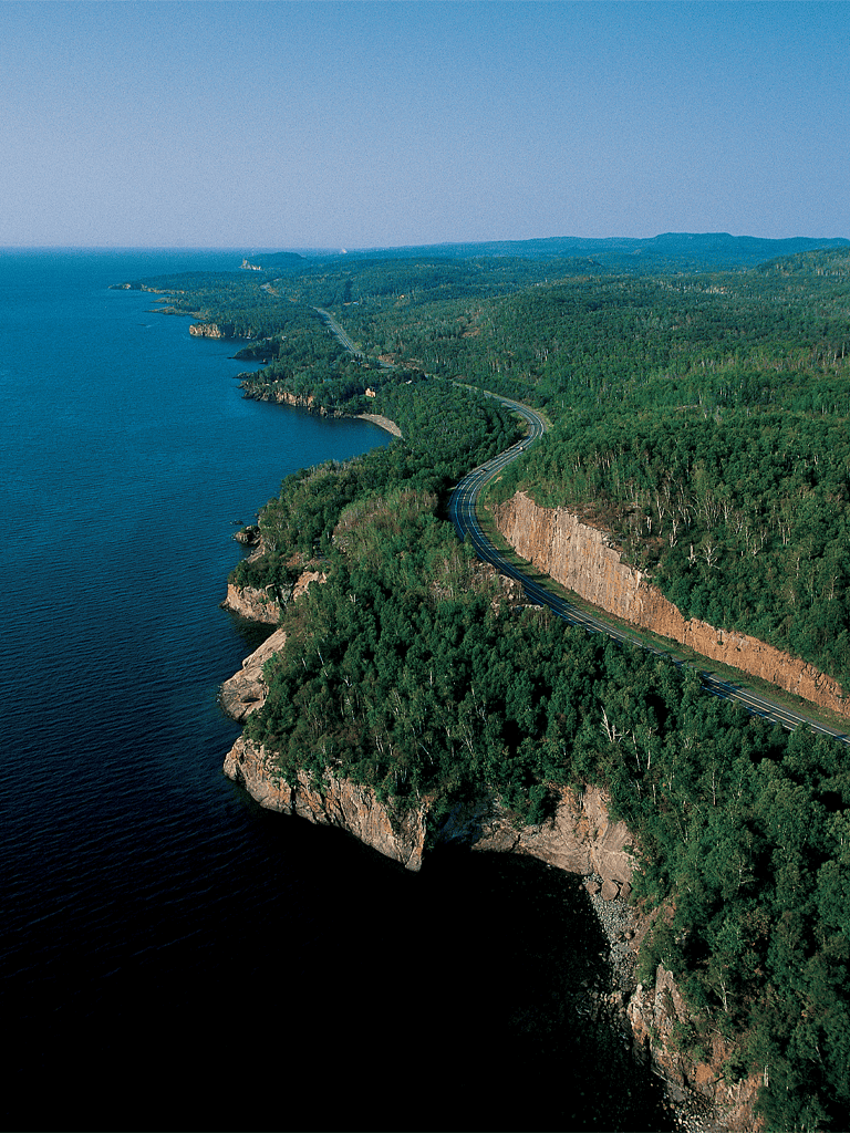 Scenic coastal highway along lush green forested cliffs overlooking the ocean.