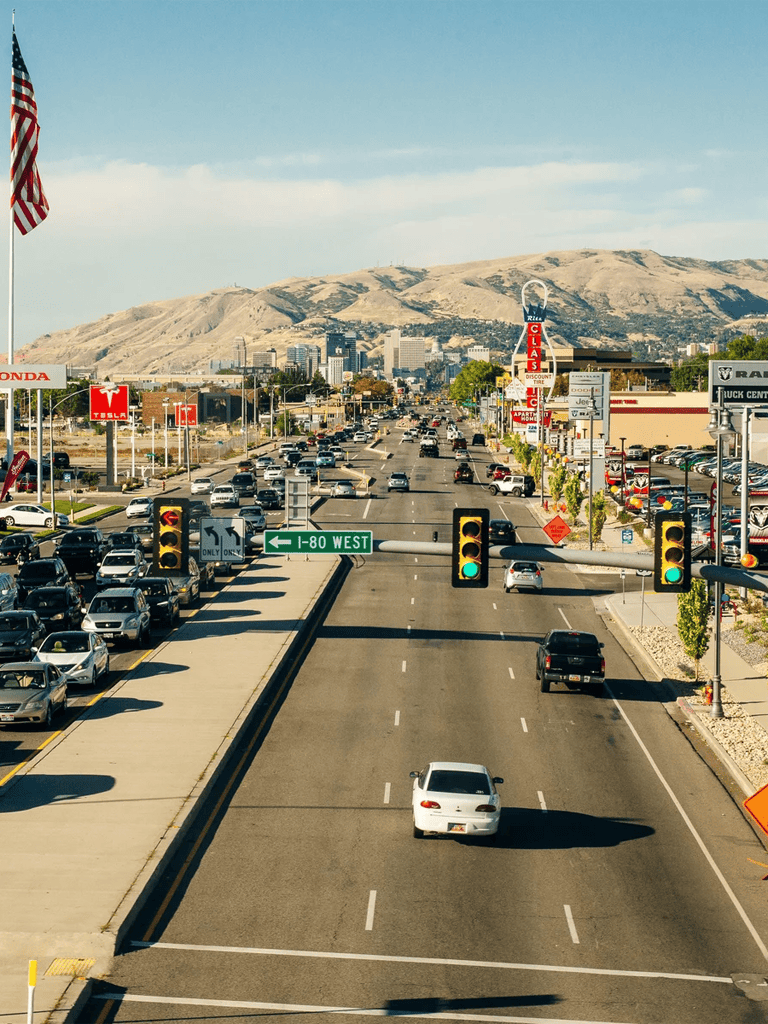 Heavy traffic on a city highway with mountains in the background, showing direction to I-80 West.