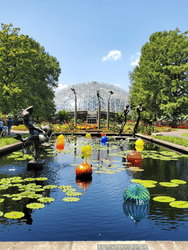 Colorful Floating Art Sculptures at Botanical Garden with Glass Geodesic Dome in Background.