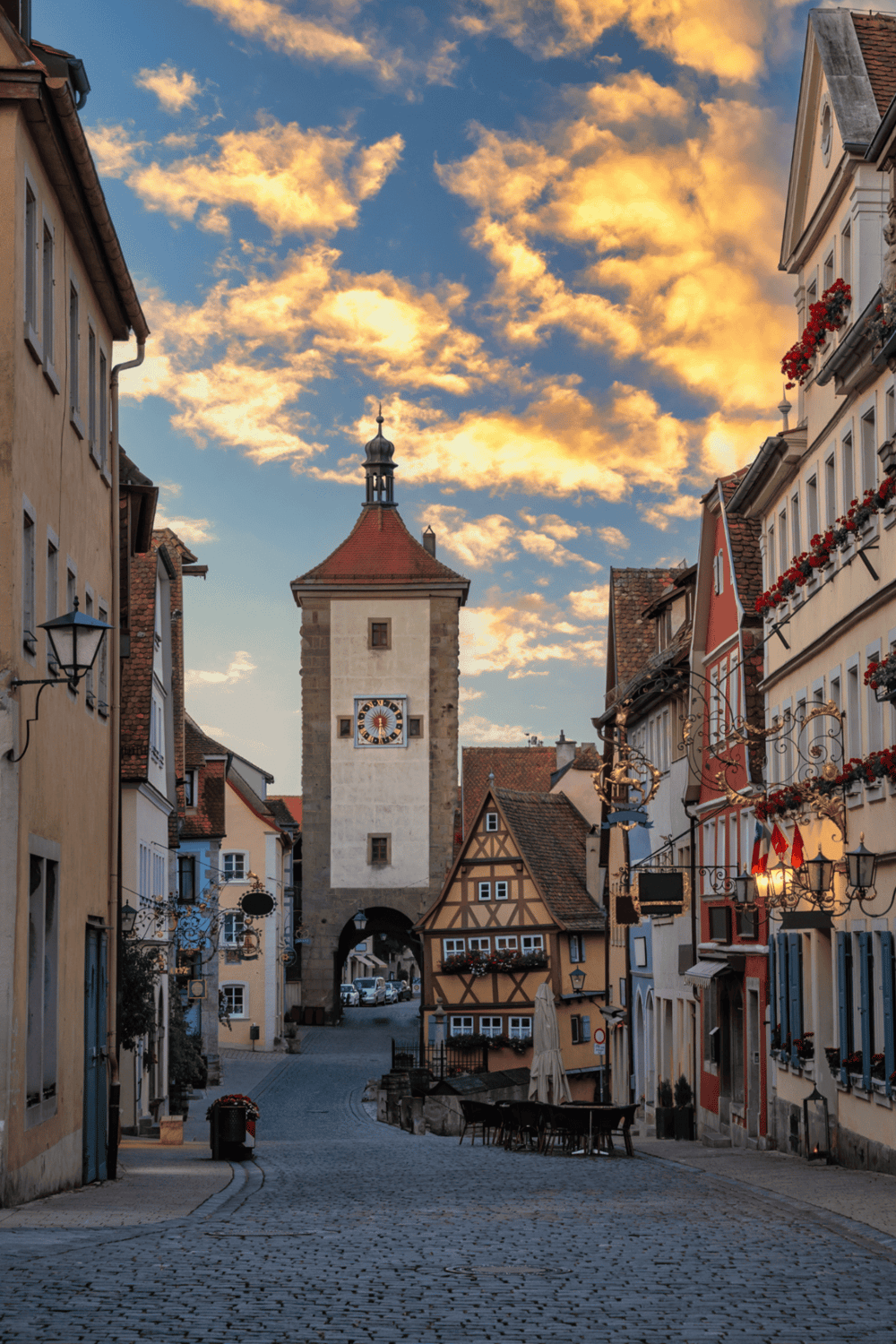 Ancient European city street with colorful buildings, cobblestone roads, and historic clock tower at sunset.