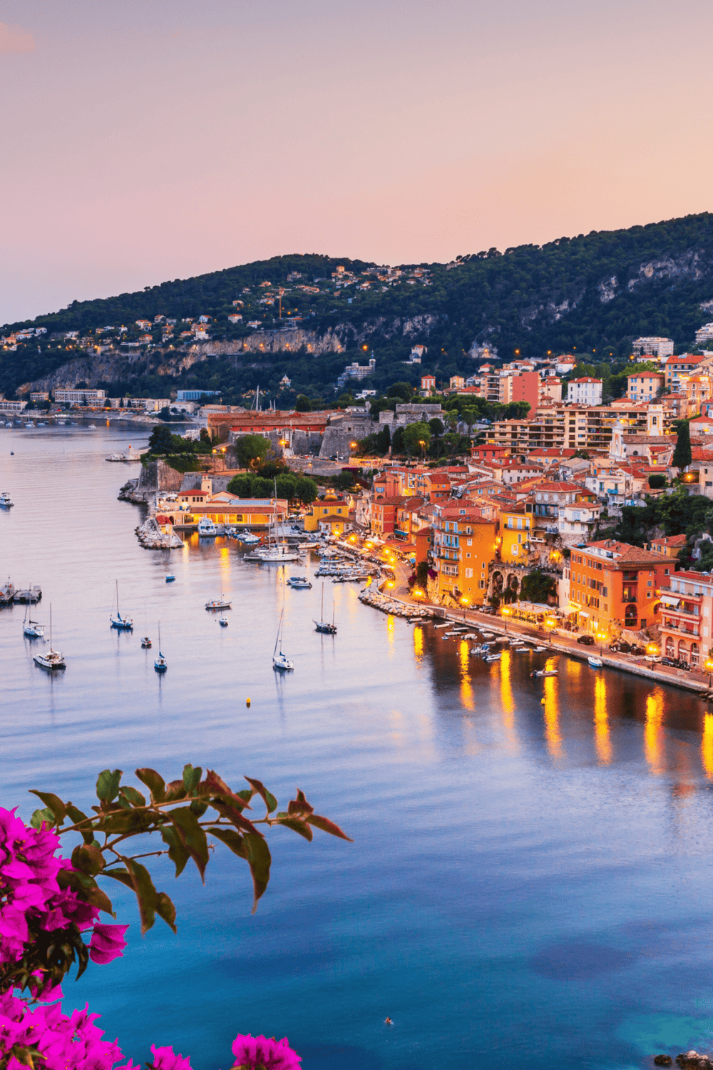 Coastal town with colorful buildings and marina at sunset.