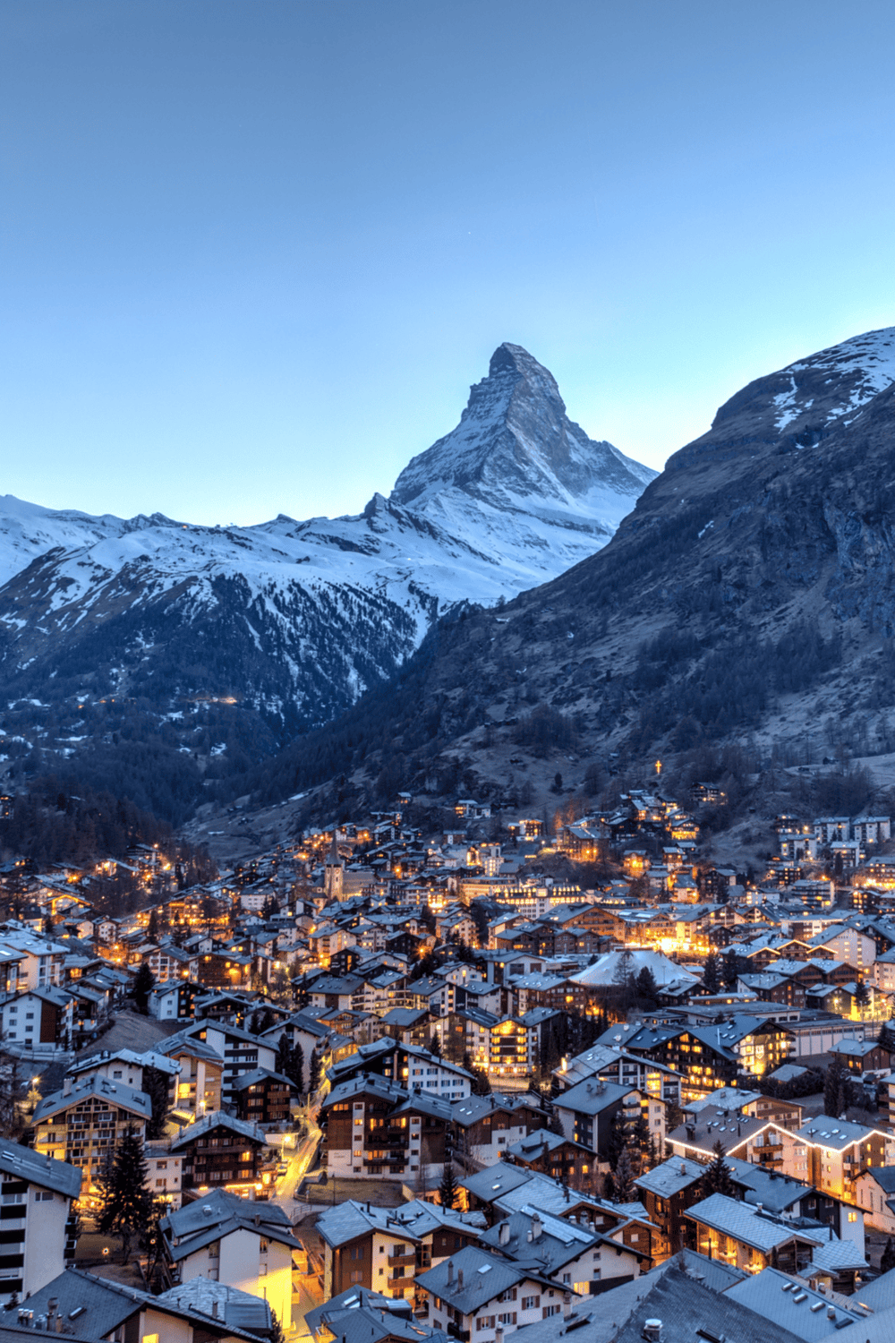 Snowy mountain village with the Matterhorn mountain in the background, illuminated buildings in a winter setting.