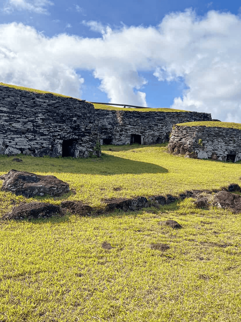 Ancient stone houses in a lush green landscape under a bright blue sky with clouds.