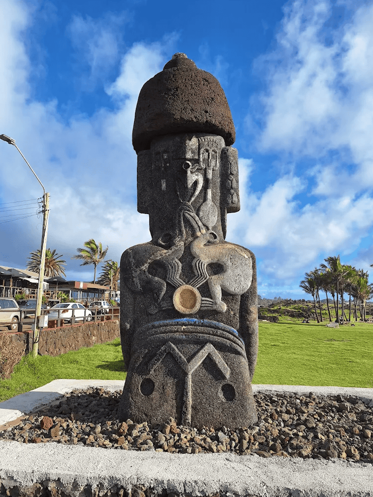 Intricate Polynesian tiki statue in outdoor park with clear blue sky and tropical palms.
