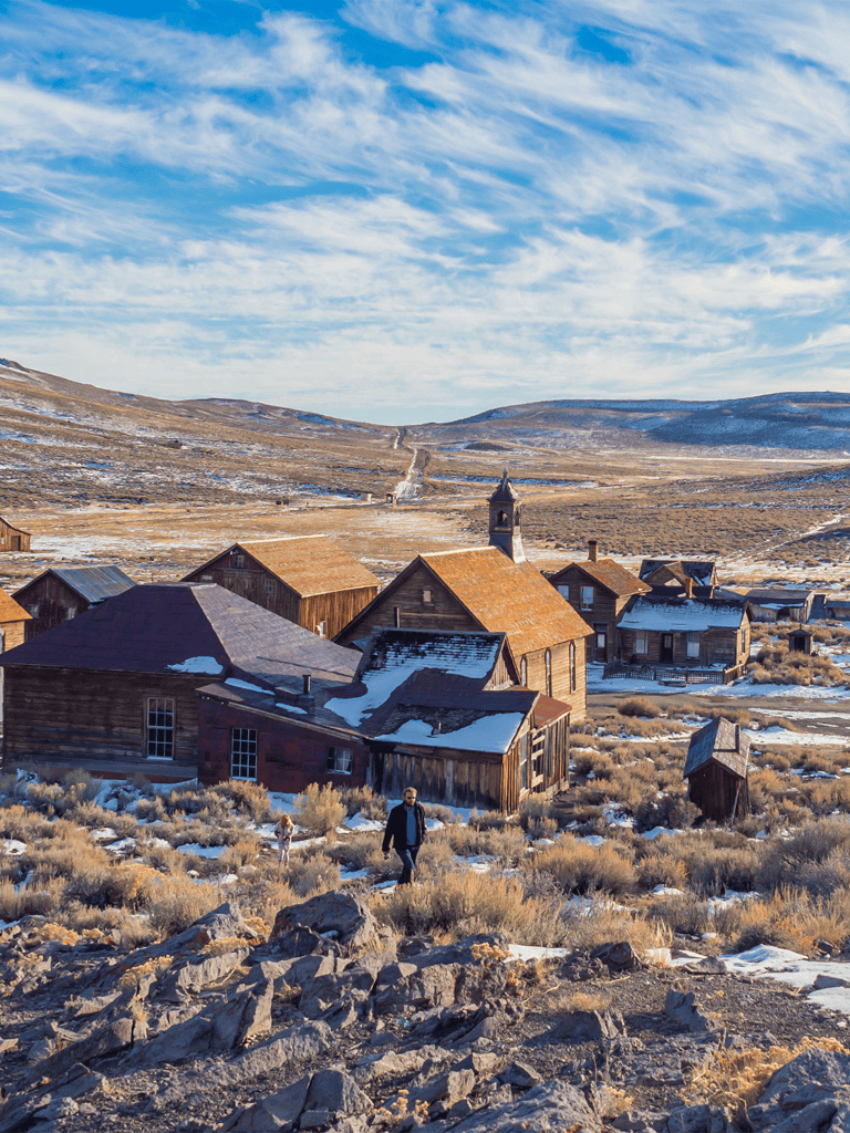 Remote mountain village with wooden houses under bright blue sky, rugged landscape, and people exploring the area.