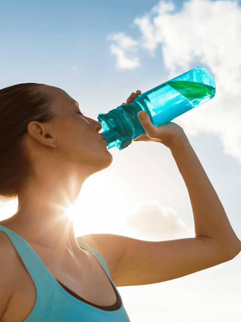Hydration during outdoor exercise, bright sky, woman drinking water, health, wellness, hydration tips.