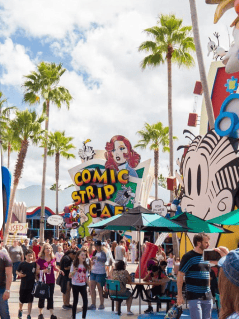 Comic strip cafe at a lively outdoor event with palm trees and large cartoon characters, perfect for family fun.